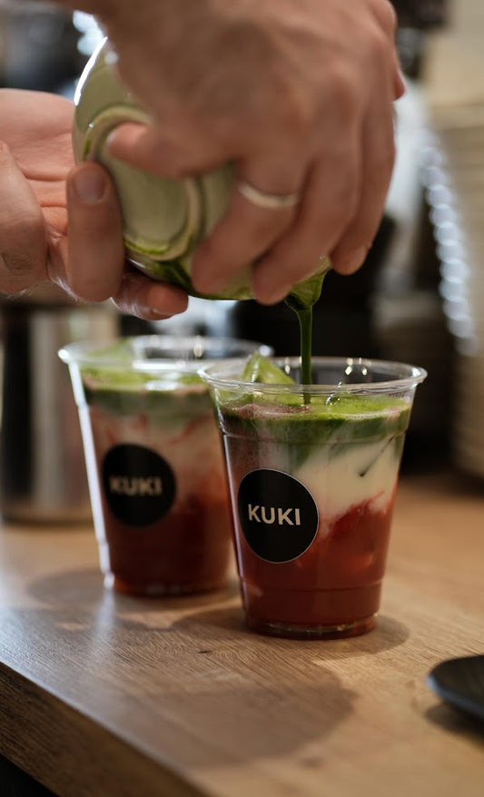 Barista gießt Matcha über einen Iced Strawberry Matcha Latte im KUKI Café