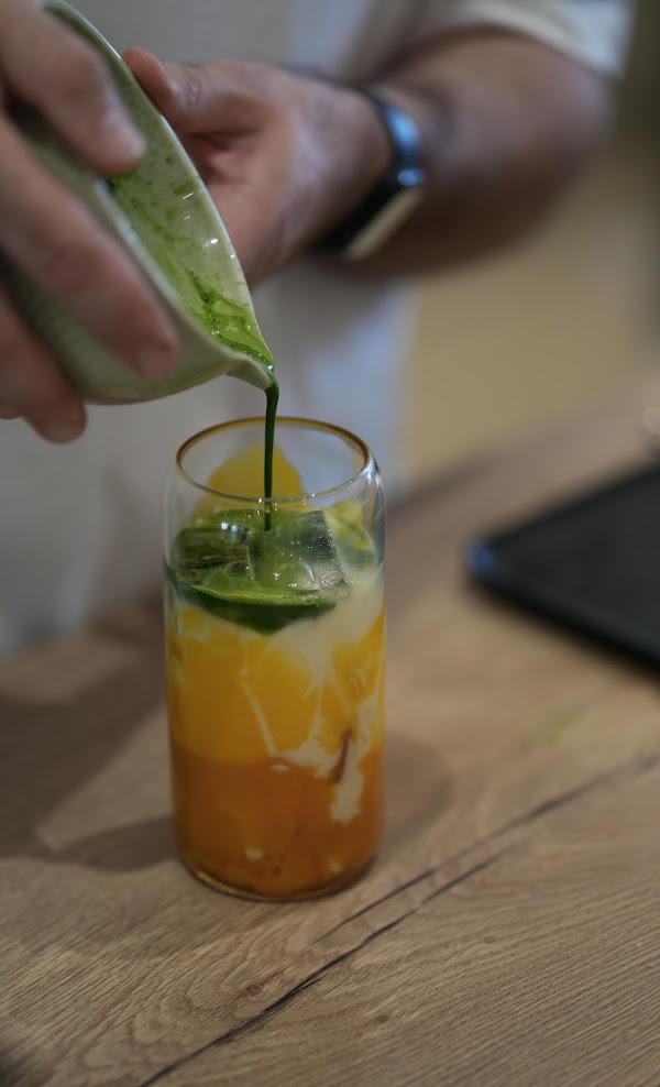 Matcha wird im Café über einen Iced Mango Latte gegossen